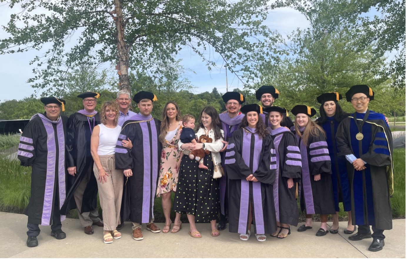 Class of 2024 graduates in black and lavender doctoral regalia with their families