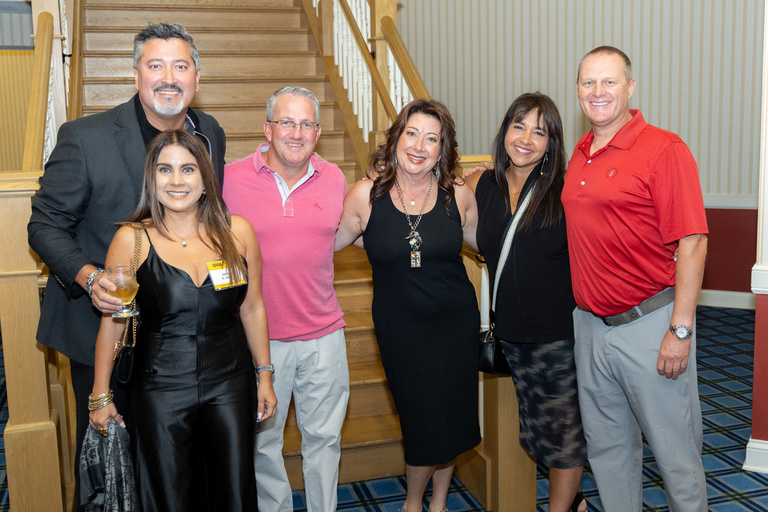 A group of alumni and their families pose for a picture at the bottom of the stairs at The Graduate Hotel.