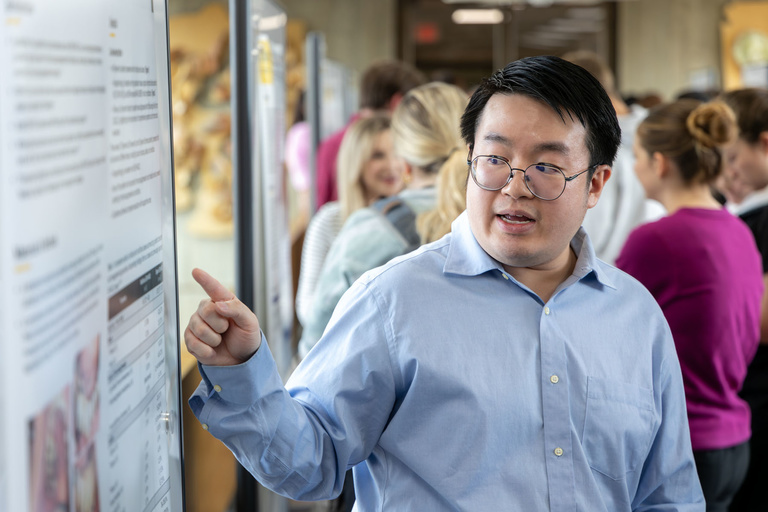 Pointing to his poster, a researcher shares their findings with research day attendees on Feb. 11, 2025.