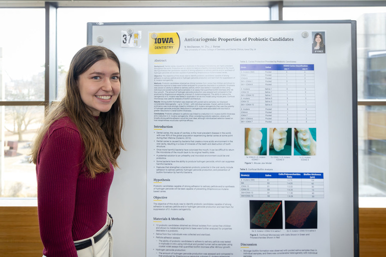 A student poses with their poster during poster presentations on the 4th-floor link.