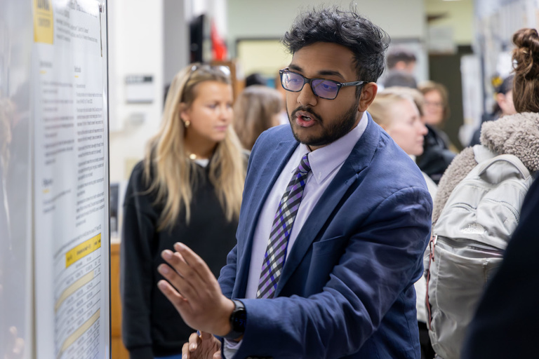 A student researcher shares their work during poster presentations on the 4th-floor link.