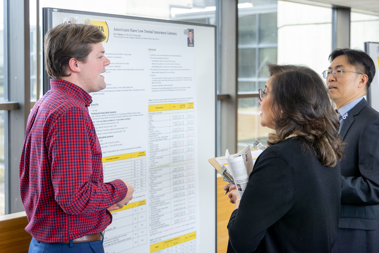 A student researcher shares their work during poster presentations on the 4th-floor link.