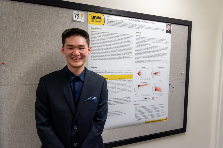 A student poses for a photo in front of their research poster on research day.