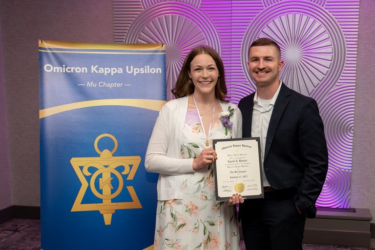 Lyndi Hunter poses for a picture in front of the OKU banner and with a certificate after being inducted into OKU.
