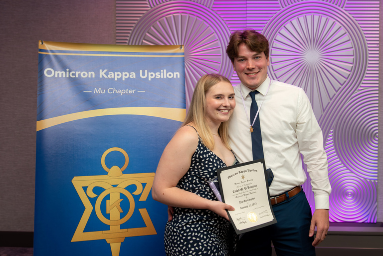 Caleb LeBorius poses for a picture in front of the OKU banner and with a certificate after being inducted into OKU.