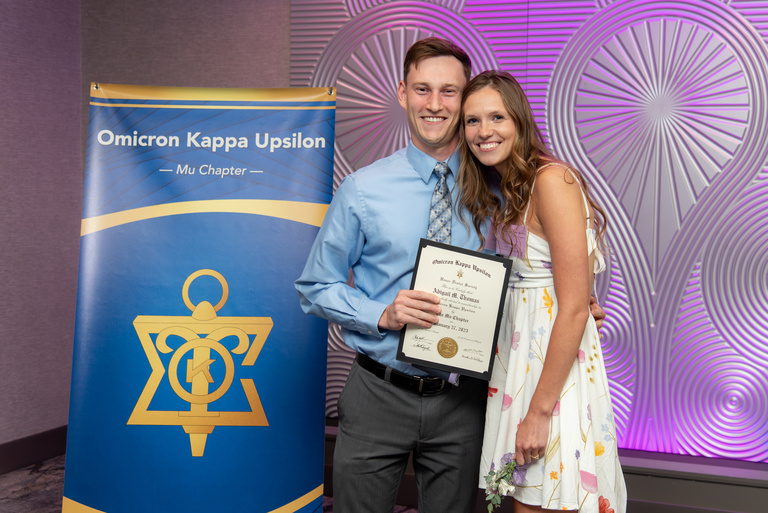 Abigail Thomas poses for a picture in front of the OKU banner and with a certificate after being inducted into OKU.