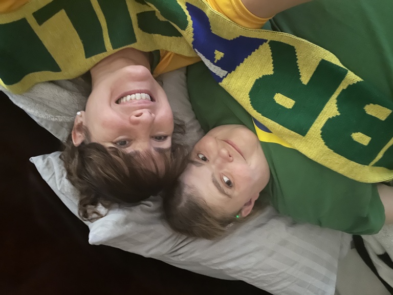 Nathalia and Karin laying down with a Brazil scarf on them.