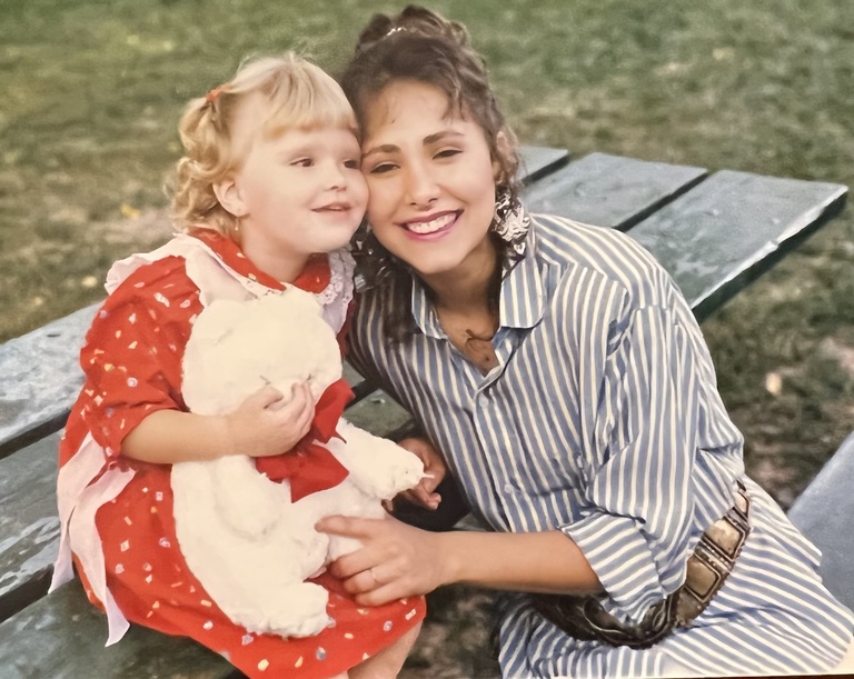 A young Karin and Nathalia take a picture together on a park bench.
