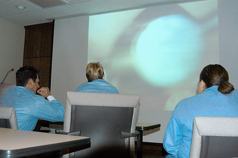 A photo of students learning from a large overhead projector showing a procedure.