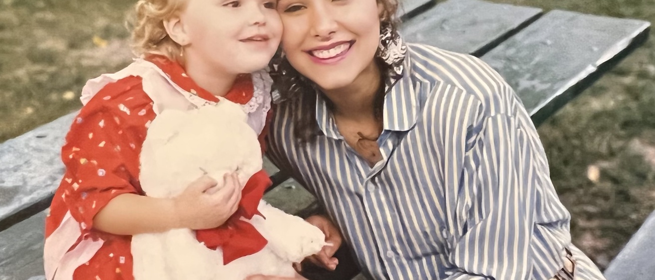 A young Karin and Nathalia take a picture together on a park bench.