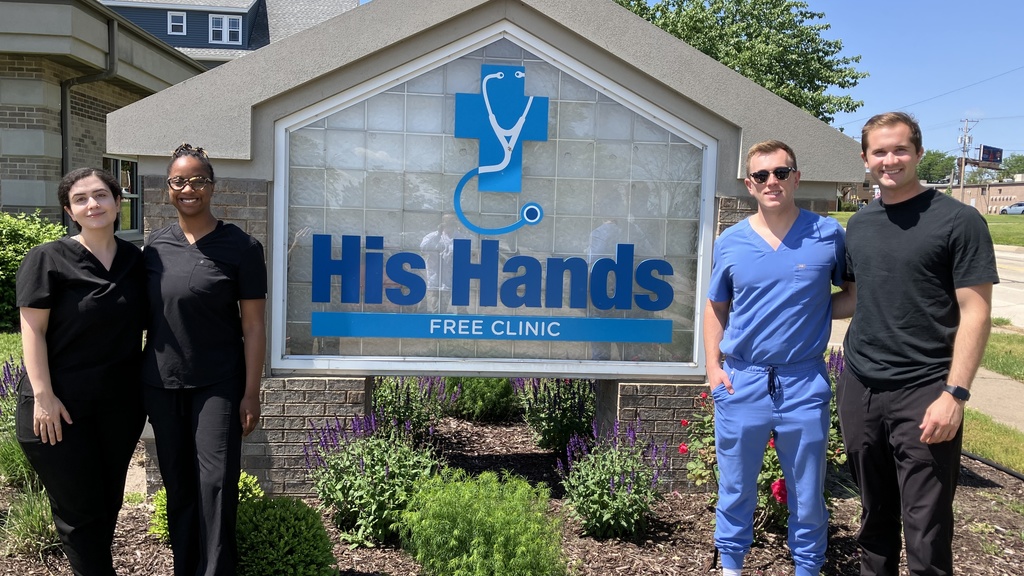 Students volunteered at His Hands Dental Clinic in Cedar Rapids. This is a picture of students posing in front of the clinic's sign.